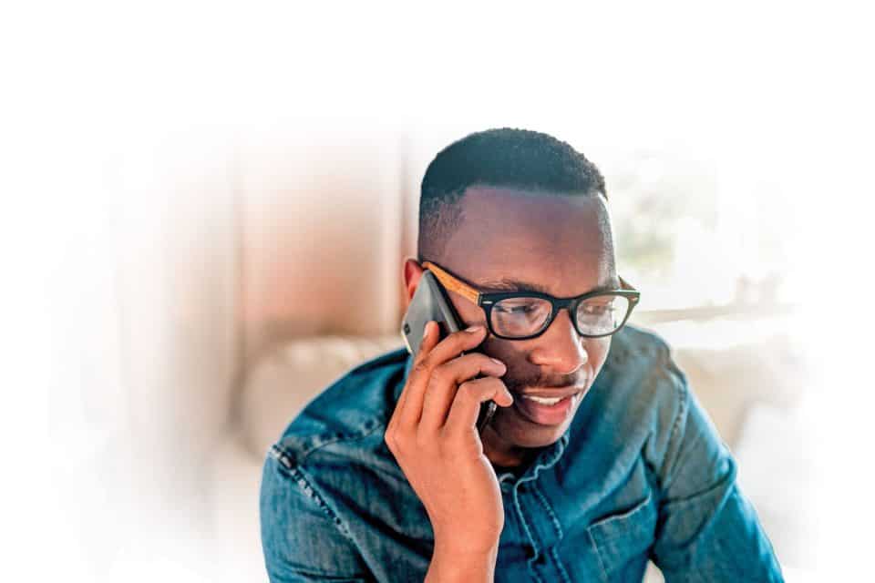 Young student talking on a phone call to a friend, colleague or family member. Black male university or college learner studying design, marketing or architecture sitting and chatting at home.